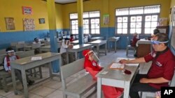 Children wearing face shield as a precaution against the new coronavirus outbreak sit spaced apart as they wait for their turn to take an admission test at Al Hidayah Islamic Elementary School in Jakarta, Indonesia, Monday, July 6, 2020. 