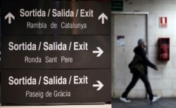 FILE - A man walks past a sign written in Catalan, Spanish and English at a train station in Barcelona.