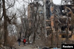 People walk past destroyed buildings in Mariupol