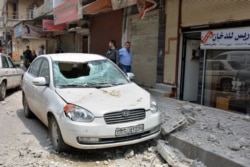 In this photo released by the Syrian official news agency SANA, people stand near a car that was damaged due to flying debris from a Syrian military base housing a weapons warehouse, in the country's central province of Homs, Syria, May 1, 2020.