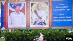 ប្រជាពលរដ្ឋម្នាក់ជិះកាត់ការតុបតែងរូបថតដើម្បីទទួលទស្សនកិច្ចផ្លូវរដ្ឋនៃប្រធានាធិបតីហ្វីលីពីនលោក រ៉ូឌ្រីហ្គូ ឌើទើតេ (Rodrigo Duterte) (រូបឆ្វេង) និងព្រះមហាក្សត្រកម្ពូជាព្រះករុណាព្រះបាទនរោត្តម សីហមុនី (រូបស្ដាំ) នៅរវាងមហាវិថីសុធារស និងមហាវិថីព្រះសីហនុ នៅថ្ងៃច័ន្ទ ទី១២ ខែធ្នូ ឆ្នាំ២០១៦ នារាជធានីភ្នំពេញ។ (ឡេង ឡែន/VOA) 