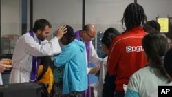 The Rev. Brian Strassburger, left, and Flavio Bravo, center, bless migrants during Mass at the Humanitarian Respite Center for migrants in McAllen, Texas, on Dec. 15, 2022. 