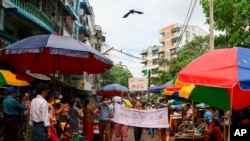 Anti-coup protesters hold signs that read "We Support NUG" that stands for ‘national unity government’ as they march on a street where vendors sell fresh products, April 17, 2021 in Yangon, Myanmar.