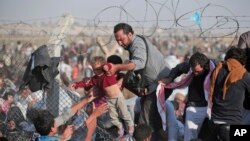 FILE - A Syrian refugee hands a toddler over a broken border fence into Turkey in Akcakale, Sanliurfa province, southeastern Turkey, June 14, 2015.