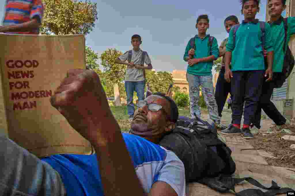 Egyptian children tease El-Hadi, a Sudanese refugee from Khartoum, while he reads his Bible. El-Hadi fled to Egypt to seek asylum. In Sudan, El-Hadi was tortured because of converting to Christianity. (H. Elrasam/VOA) 