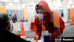 Seorang pemilih muda mengisi surat suara dibantu oleh petugas pemungutan suara di tempat pemungutan suara di mal Midtown Center, Milwaukee, pada hari pertama pencoblosan langsung, di Wisconsin, 20 Oktober 2020. (Foto: Reuters) 