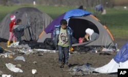FILE - A boy walks through mud in an improvised camp on the border line between Macedonia and Serbia near northern Macedonian village of Tabanovce, Tuesday, March 8, 2016.