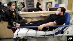 Donnie Cardenas, right, waits in an emergency room hallway alongside roommate Torrey Jewett, left, as he recovers from the flu at the Palomar Medical Center in Escondido, Calif., Jan. 10, 2018.