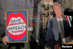FILE - An opponent of U.S. President Donald Trump carries a sign about impeachment next to a supporter with a cardboard cutout in Boston, Massachusetts, Jan. 19, 2019.