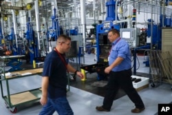 In this Oct. 24, 2017, photo, workers pass along industrial machines at Lord Corporation, a manufacturer of industrial coatings, adhesives, bearings, and sensing equipment for range of commercial markets, including United States military contracts