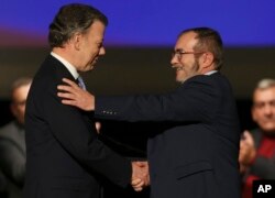 FILE - Colombia's President Juan Manuel Santos, left, shakes hands with Rodrigo Londono, known as Timochenko, top leader of the Revolutionary Armed Forces of Colombia, FARC, after signing a revised peace pact at Colon Theater in Bogota, Colombia, Nov. 24, 2016.