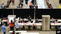 FILE - People work near refrigerators used to store the Pfizer vaccine for COVID-19, as patients who have received the shot sit in an observation area at a clinic in an Amazon.com facility in Seattle, Jan. 24, 2021.