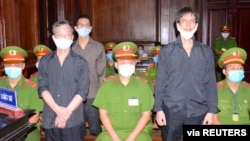 អ្នក​កាសែត​របស់​សមាគម​អ្នក​កាសែត​ឯករាជ្យ​វៀតណាម លោក Pham Chi Dung​ (ស្ដាំ) លោក Le Huu Minh Tuan (កណ្ដាល) និង​លោក​ Nguyen Tuong Thuy (ឆ្វេង) ឈរ​នៅ​ចន្លោះ​ប៉ូលិស ក្នុង​អំឡុងពេល​នៃ​សវនាការ​របស់​ពួកគេ​នៅ​ទីក្រុង​ហូជីមិញ ប្រទេស​វៀតណាម ថ្ងៃទី៥ ខែមករា ឆ្នាំ២០២១។