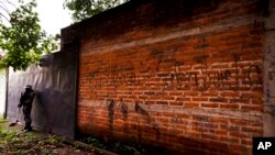 FILE - In this Oct. 10, 2019, file photo police guard next to a graffiti wall with the name of a gang as part of a routine patrol in Lourdes, La Libertad, El Salvador. (AP Photo/Eduardo Verdugo, File)