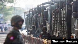 Soldiers stand next to military vehicles as people gather to protest against the military coup, in Yangon, Aug. 21, 2021.