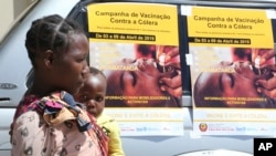 Une femme et son bébé passent devant les affiches de la campagne de vaccination contre le choléra dans un camp de déplacés à Beira, au Mozambique, le 3 avril 2019. 