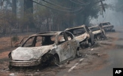FILE - Burned cars left by their drivers sit along a road in Paradise, California after a wildfire burned much of the town in November of 2018.