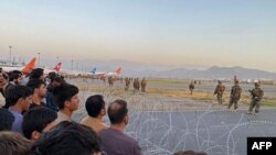 Afghans (L) crowd at the airport as US soldiers stand guard in Kabul on August 16, 2021
