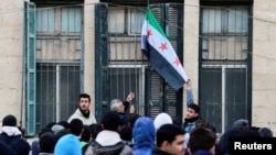 A teacher hoists the flag adopted by the new Syrian rulers at a school in the early morning, following an announcement of the reopening of schools by the authorities, after the ousting of Syria’s Bashar al-Assad, in Damascus, Dec. 15, 2024. 