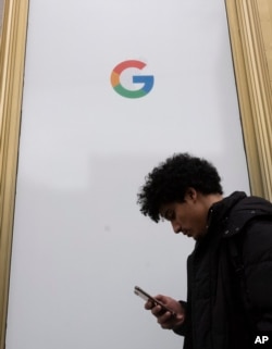 A man using a mobile phone walks past Google offices, Monday, Dec. 17, 2018, in New York. (AP Photo/Mark Lennihan)