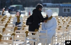 A woman puts a scarf on a statue of a comfort woman sitting in a installation of empty chairs symbolizing the victims in Seoul, South Korea, Dec. 27, 2017.