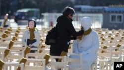 A woman puts a scarf on a statue of a comfort woman sitting in an installation of empty chairs symbolizing the victims in Seoul, South Korea, Dec. 27, 2017. 