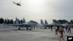 Russian Su-30 jets are parked at an airbase in Syria, on Oct. 22, 2015, as a Mi 24 helicopter gunship flies overhead. 