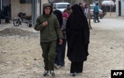FILE - A Kurdish female fighter, left, walks next to a woman, reportedly the wife of an Islamic State (IS) group fighter, at the Internally Displaced Persons (IDP) camp of al-Hol in al-Hasakeh governorate in northeastern Syria, Feb. 7, 2019.
