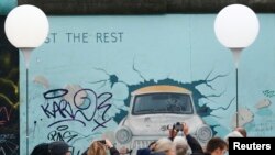 (រូបភាព​ឯកសារ)​ មនុស្ស​ដើរកាត់​ និងថត​រូបភាព​ក្បែរ​កន្លែង​តាំង​'Lichtgrenze' ព្រំដែន​នៃពន្លឺ តាម​បណ្តោយ​សាល​កម្រង​រូបភាព​ផ្នែកខាង​កើត ដែល​ជាតំបន់​មាន​ផ្នែក​ជញ្ជាំង​បែរឡាំង​ធំជាងគេ​បង្អស់​សេសសល់​ ក្នុងរដ្ឋធានី​បែរឡាំង​ ប្រទេស​អាល្លឺម៉ង់​ ថ្ងៃទី៩​ ខែ​វិច្ឆិកា ឆ្នាំ​២០១៤។ 