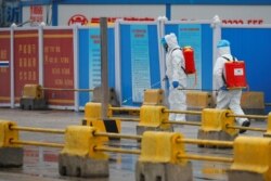 FILE - Workers in PPE spray the ground with desinfectant in Baishazhou market during a visit of World Health Organization (WHO) team tasked with investigating the origins of the coronavirus (COVID-19) pandemic, in Wuhan