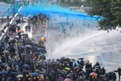 FILE - Pro-democracy protesters react as police fire water cannons outside the government headquarters in Hong Kong.