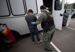 FILE - An U.S. Immigration and Customs Enforcement officer transfers a man in hand and ankle cuffs onto a van during an operation in Escondido, Calif., July 8, 2019.
