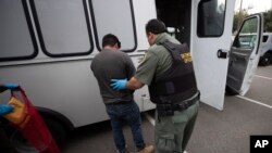 FILE - An U.S. Immigration and Customs Enforcement (ICE) officer transfers a man in hand and ankle cuffs onto a van during an operation in Escondido, California, July 8, 2019.