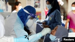 FILE - A medical worker collects a swab sample from a Top Glove worker to be tested for the COVID-19 outside a hostel under enhanced lockdown in Klang, Malaysia, Nov. 18, 2020. 