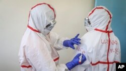 FILE - A nurse writes on the protective clothing of fellow nurse Lucy Kanyi, right, with her name so she can be recognized when wearing it and the time of day, at the infectious disease unit of Kenyatta National Hospital, Nairobi, Kenya, March 6, 2020.
