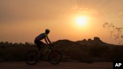 A cyclist bikes past the setting sun at Papago Park during a heatwave where temperatures hit 46 degrees Celsius Tuesday, June 15, 2021, in Phoenix. (AP Photo/Ross D. Franklin)