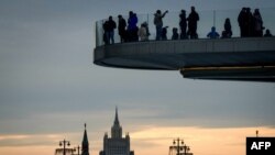 FILE - People enjoy the view from a pedestrian bridge in the Zaryadye Park, with the Kremlin's towers and the Russian Foreign Ministry headquarters seen in the background, in Moscow on March 13, 2018.