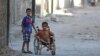 FILE - Boys, one of them in a wheelchair, venture down a street in the al-Sheikh Said neighborhood of Aleppo, Syria, Sept. 1, 2016. 