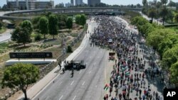 A demonstrator waves the flag of Palestine as police officers guard outside the Federal Building during a protest against Israel and in support of Palestinians, May 15, 2021, in the Westwood section of Los Angeles. 