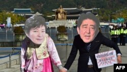 FILE - Protesters wearing masks depicting South Korean President Park Geun-Hye (L) and Japanese Prime Minister Shinzo Abe (R) hold hands during an anti-Japanese rally in Seoul. South Korea President Park Geun-hye and Japanese Prime Minister Shinzo Abe promised to resolve the long-standing dispute over comfort women by year’s end.
