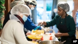 Chief coordinator Glenda Andrew, right, speaks with members of the Preston Windrush Covid Response team as they dish out West Indian meals for delivery, at the Xaverian Sanctuary, in Preston, England, Friday Feb. 19, 2021. (AP Photo/Jon Super)