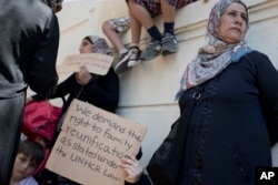 FILE - Stranded migrants and refugees, most of them from Syria, hold placards as they protest outside the German Embassy in Athens, July 19, 2017.