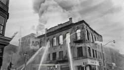 资料照片 - 消防员将水流引向新泽西州纽瓦克王子街和法院街拐角的一座着火的建筑，在那里持续了四天的致命暴力和抢劫后来被称为纽瓦克骚乱。（1967年7月15日）(美联社照片/马蒂·莱德汉德，档案)