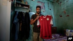 In this May 9, 2020 photo, 28-year-old defender Mahrous Mahmoud holds up his Egyptian national football team jersey he trains with, inside his home, in Manfalut, a town 350 kilometers (230 miles) south of Cairo in the province of Assiut, Egypt. (AP Photo/Nariman El-Mofty)