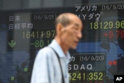 A man walks past an electronic stock board showing Japan's Nikkei 225 index, left, that fell 80.18 points or 0.5 percent to 16,411.97 at a securities firm in Tokyo, Sept. 21, 2016.