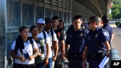 FILE - U.S. Customs and Border Patrol officials wait to hand asylum seekers over to Mexican officials as they are returned under the so-called Remain in Mexico program, on the international bridge between Laredo, Texas, and Nuevo Laredo, Mexico, July 10, 