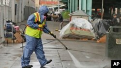 In this Feb. 26, 2016 file photo, a city worker uses a power washer to clean the sidewalk by a tent city along Division Street in San Francisco. 