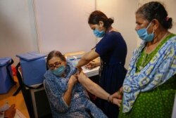 An elderly woman, left, holds the arm of her domestic helper as she receives Covishield vaccine against the coronavirus at a vaccination center in Mumbai, India, June 22, 2021.