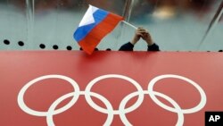 Seorang penonton memegang bendera Rusia di atas foto Cincin Olympiade di Adler Arena Skating Center di Olimpiade Musim Dingin di Sochi, Rusia, 18 Februari 2014. (Foto: David J. Philip/AP)
