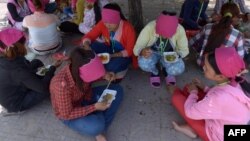 រូបឯកសារ៖ កម្មករ​រោងចក្រ​កាត់​ដេរ​សម្លៀកបំពាក់​កម្ពុជា​កំពុង​ទទួល​ទាន​អាហារ​ពេល​ថ្ងៃ​ត្រង់​នៅ​ក្រោម​ដើម​ឈើ​មួយ​ដើម នៅ​ខាង​មុខ​រោងចក្រ​ដែល​ពួកគេ​ធ្វើការ ភ្នំពេញ ថ្ងៃទី៨ ខែឧសភា ឆ្នាំ២០១៤។ 